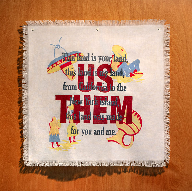 Ann Morton, US | THEM, 2020. Vintage Morton family tablecloth, acrylic paint, new embroidery. Photo credit: Bill Timmerman. Many times, for a summer meal of hamburger tacos, my mother would use this tablecloth on our dining room table. We thought nothing of the American-made references to Mexican stereotypes depicted on this cloth as we ate our American version of "Mexican food". We thought nothing.